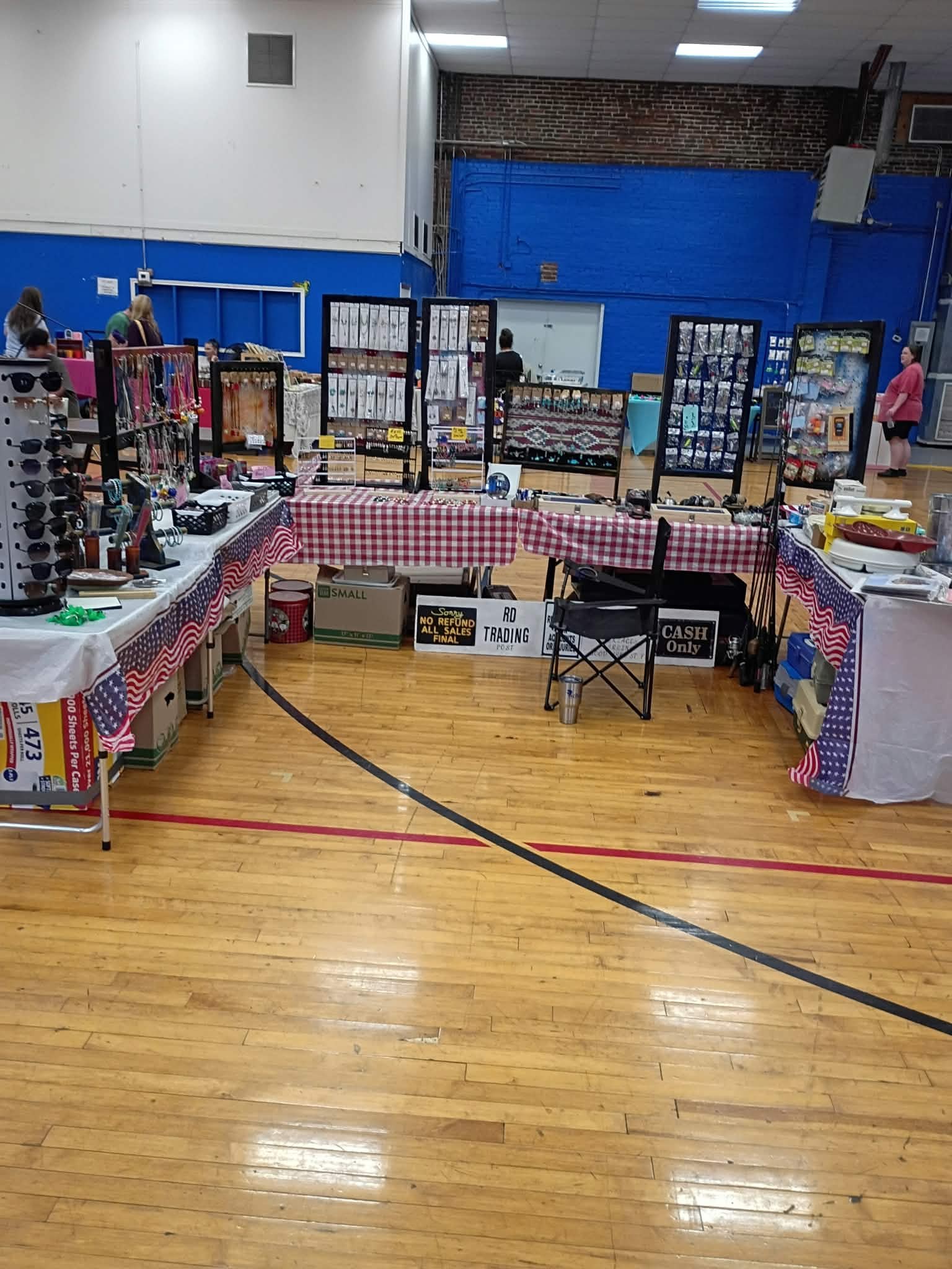 The R D Trading post tables at an indoor show, with jewelry racks, sunglasses and tackle